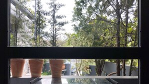 A room with a glass table and two chairs, overlooking a garden with trees and potted plants. - Mona Lisa Guest House (Volos)