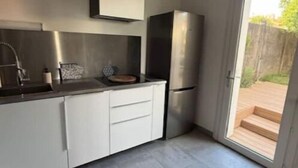 Une cuisine moderne avec des armoires blanches, des appareils en acier inoxydable et une porte-fenêtre coulissante donnant sur un espace extérieur.