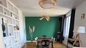 Un salon moderne avec un plancher en bois, une table à manger avec des chaises, un canapé, un luminaire suspendu et une étagère blanche.