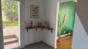Une pièce dotée d’un sol carrelé, d’un banc en bois, d’une étagère murale ornée d’objets décoratifs et d’une porte donnant sur un espace extérieur.