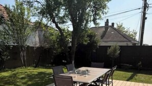 Une terrasse en bois avec une table et des chaises, entourée d’une pelouse et d’arbres.