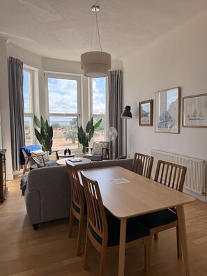Un coin repas avec une table et des chaises en bois, un canapé, un ventilateur et de grandes fenêtres avec des rideaux.