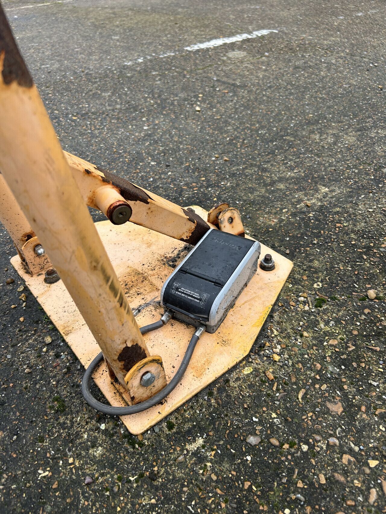 Un appareil mécanique doté d’une unité de commande noire et d’une base en bois, posé sur une surface rugueuse.