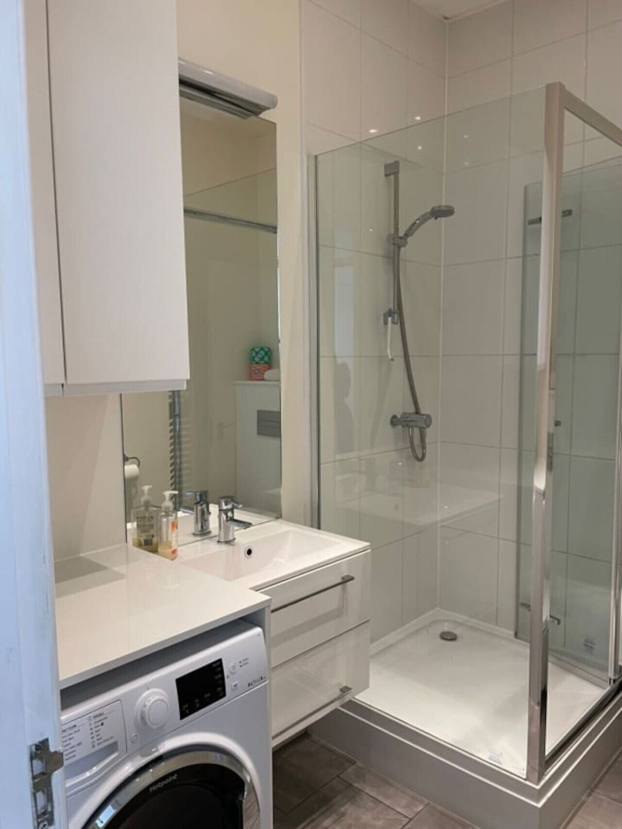A modern bathroom with a glass-enclosed shower, a built-in washing machine, and a large mirror.