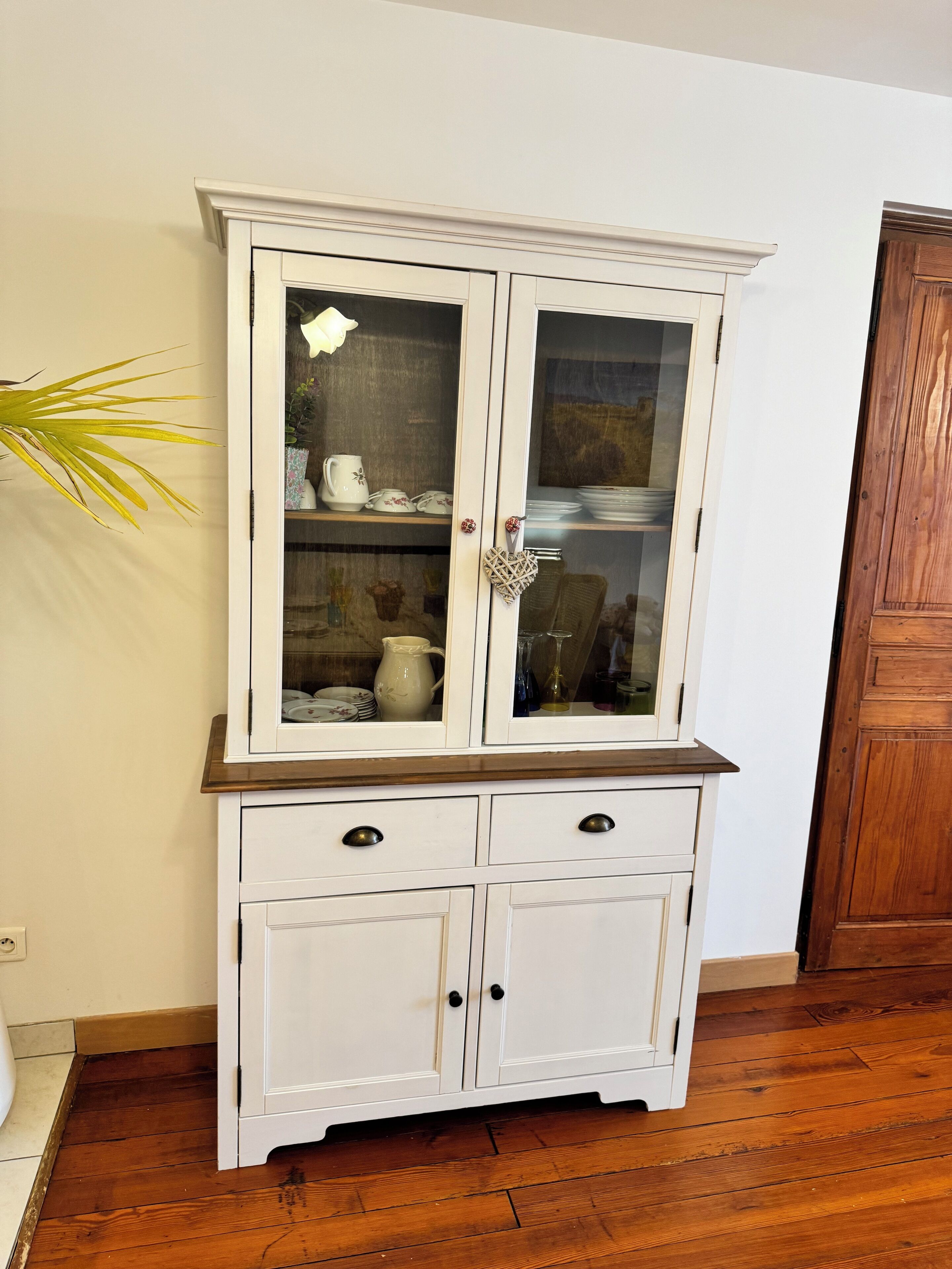 Een witte houten kast met glazen deuren, twee lades en een houten aanrechtblad.