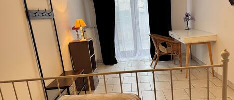 Un dormitorio con cama, escritorio, silla, radiador y ventana con cortinas.