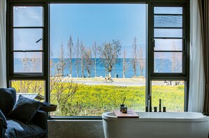 Een kamer met een groot raam, met uitzicht op een meer en bomen.