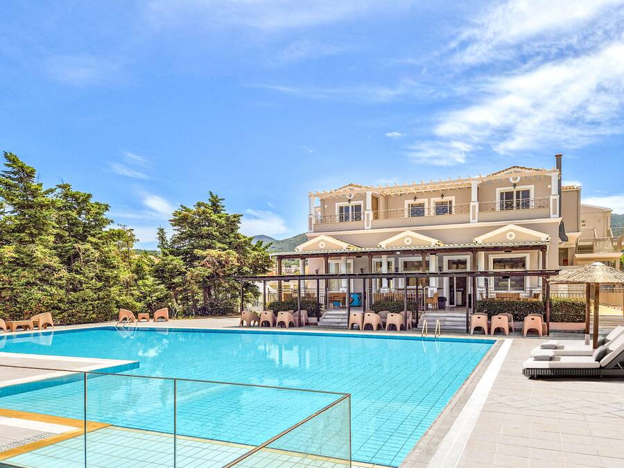 Una piscina con sillas de descanso y un edificio con balcón al fondo.
