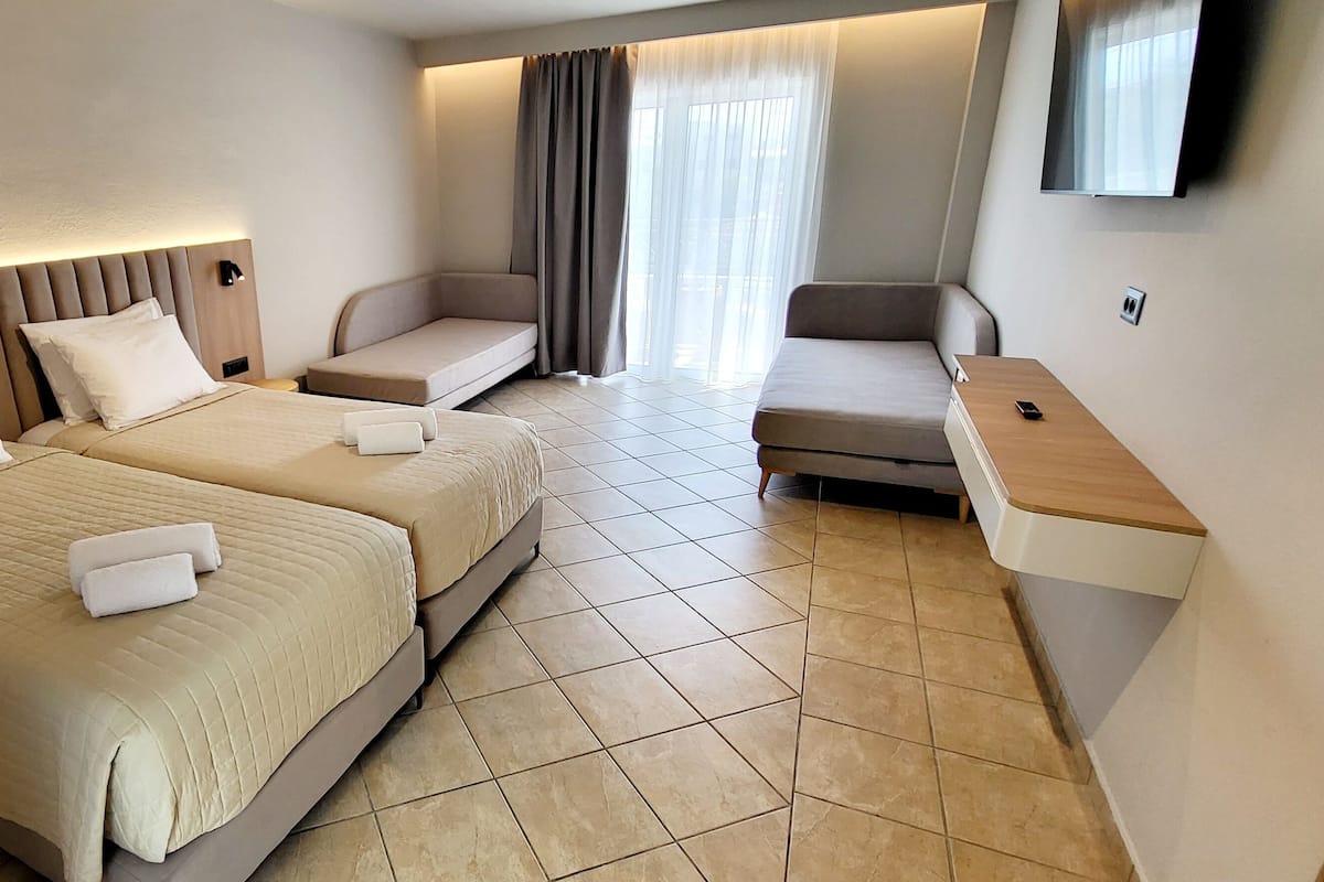 Una habitación de hotel con dos camas, un sofá, un televisor y una mesita.
