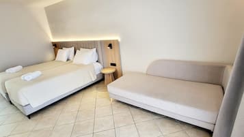 A hotel room with two beds, a sofa, and a bedside table.