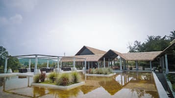 A resort with outdoor seating, a pool, and a thatched-roof structure.