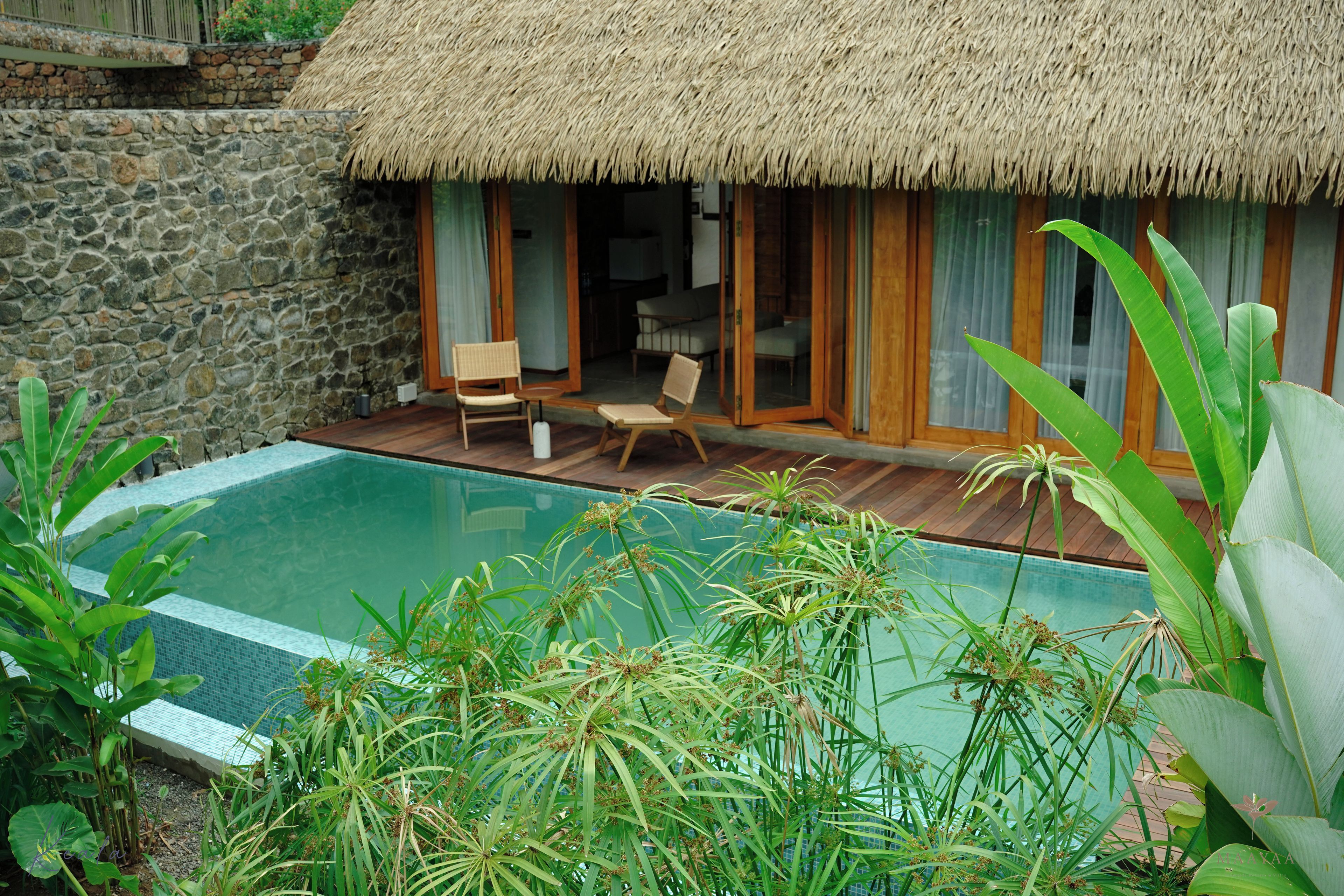 A poolside area with a thatched-roof structure, stone walls, and a pool.