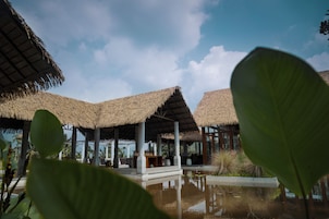 Un resort con edificaciones de techo de paja, una piscina y abundante vegetación.