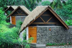 A bungalow with thatched roofs, stone walls, and a wooden door. - Maayaa riverside villa by KPM Tripenta (Mannarkkad)