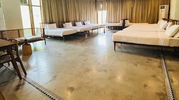 A spacious hotel room with a large bed, two smaller beds, a sofa, and a dining table.