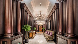 A grand hallway with tall wooden columns, a chandelier, and a sofa with cushions. - Paris Hotel (Shanghai)