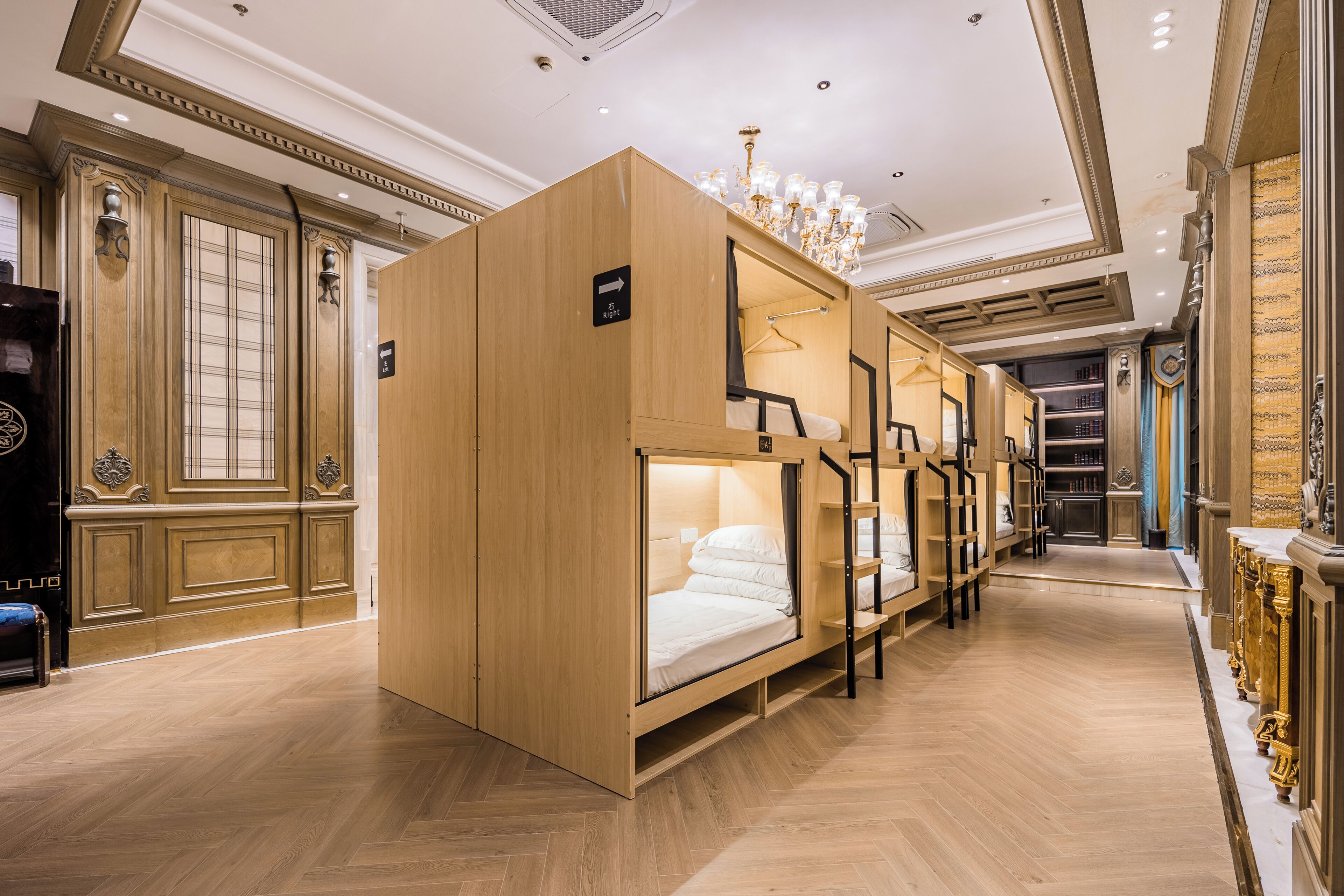 Habitación de hotel con literas, paneles de madera, una araña y una estantería.