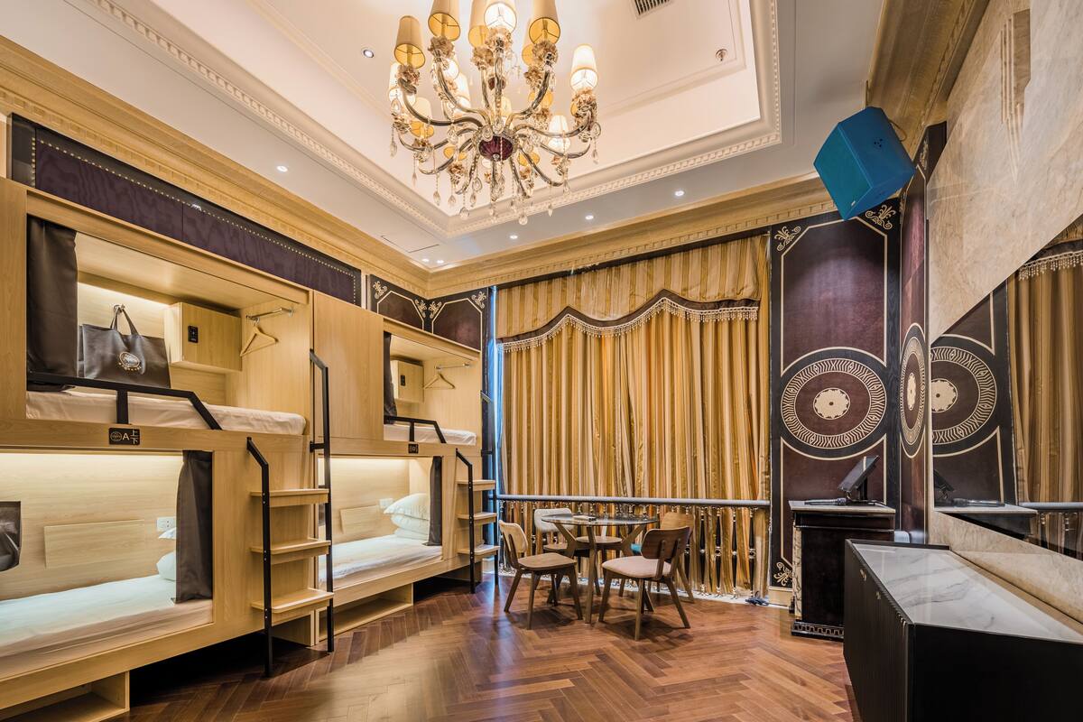 A hotel room with bunk beds, a dining area with chairs and a table, and a chandelier.