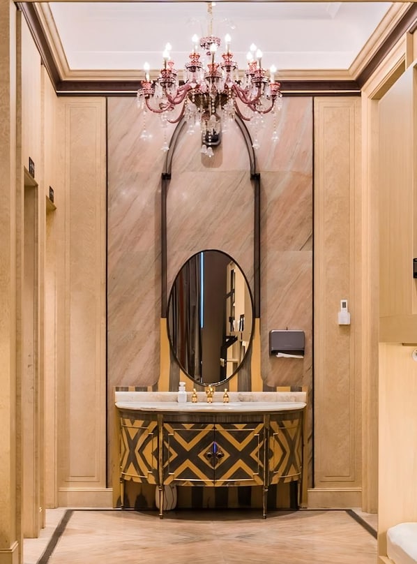Une salle de bain luxueuse dotée d’un grand miroir, d’un meuble-lavabo en marbre, d’un lustre et d’un design moderne.