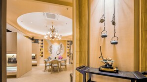 A hotel room with a wooden floor, a dining area with a table and chairs, a chandelier, and a wall-mounted shelf with decorative items. - Paris Hotel (Shanghai)