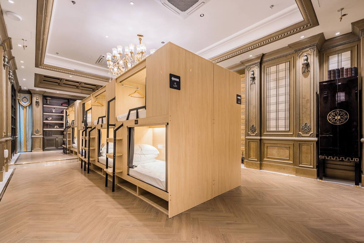 A hotel room with a wooden bunk bed, a chandelier, and a black wardrobe.