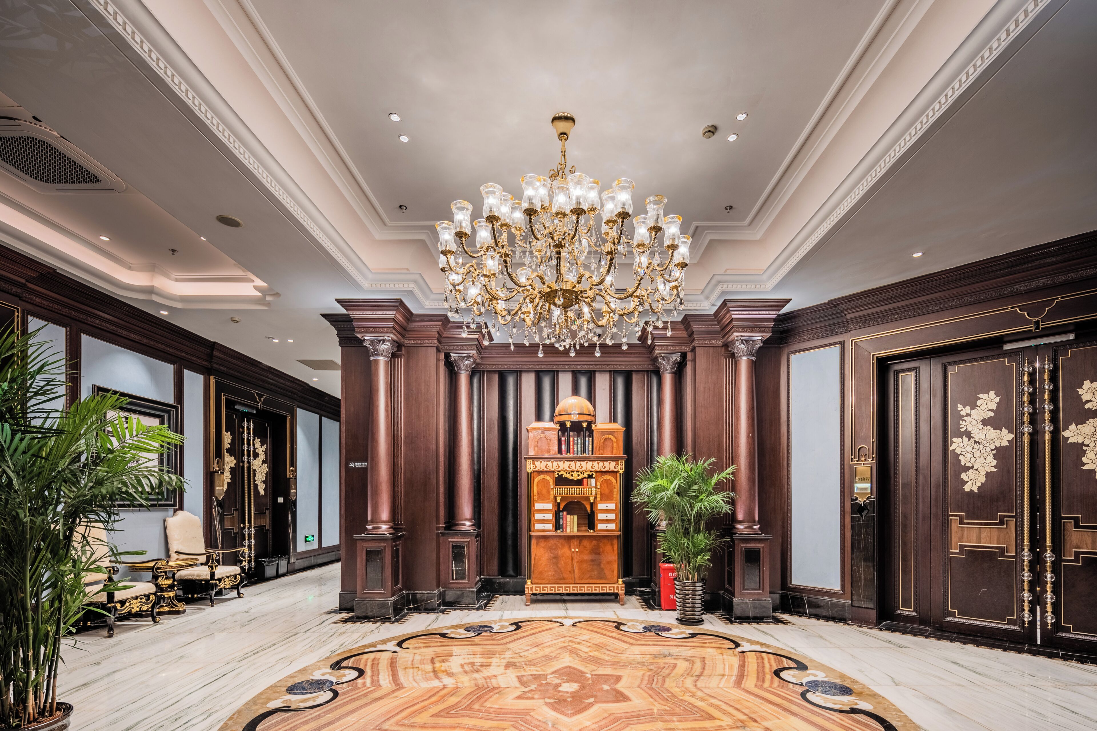 A grand lobby with a large chandelier, ornate wooden paneling, and a central decorative piece.