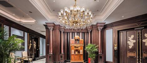 A grand lobby with a large chandelier, ornate wooden paneling, and a central decorative piece.