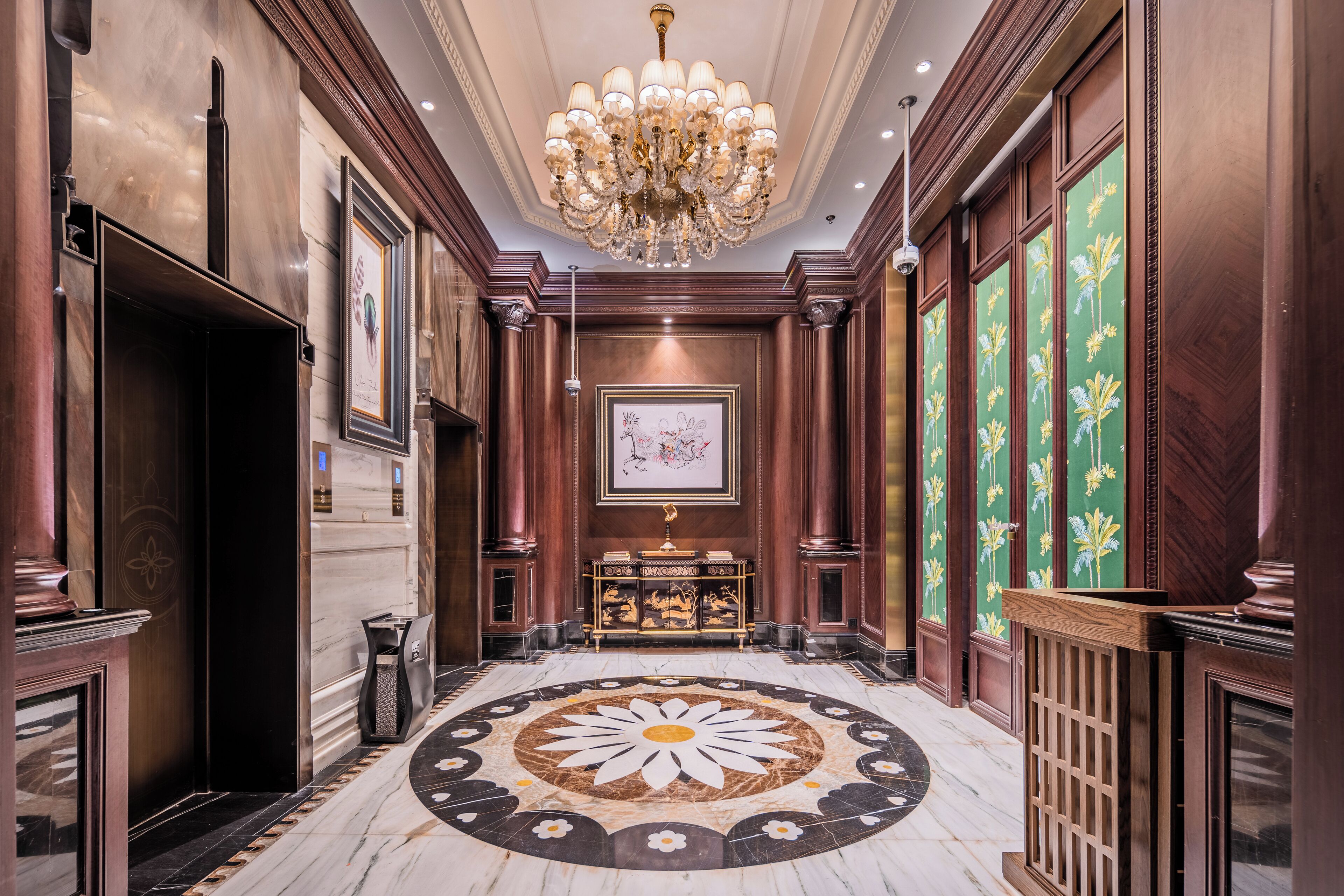 A grand hallway with a marble floor, a large chandelier, and framed artwork on the walls.