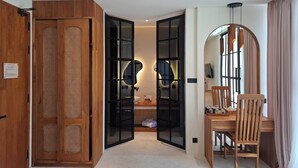 A room with a wooden wardrobe, a desk with a chair, a mirror, and a television. - OhJulia Hotel Komodo (Labuan Bajo)