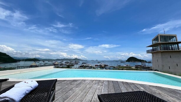 A poolside area with lounge chairs and a view of the sea and boats. - OhJulia Hotel Komodo (Labuan Bajo)
