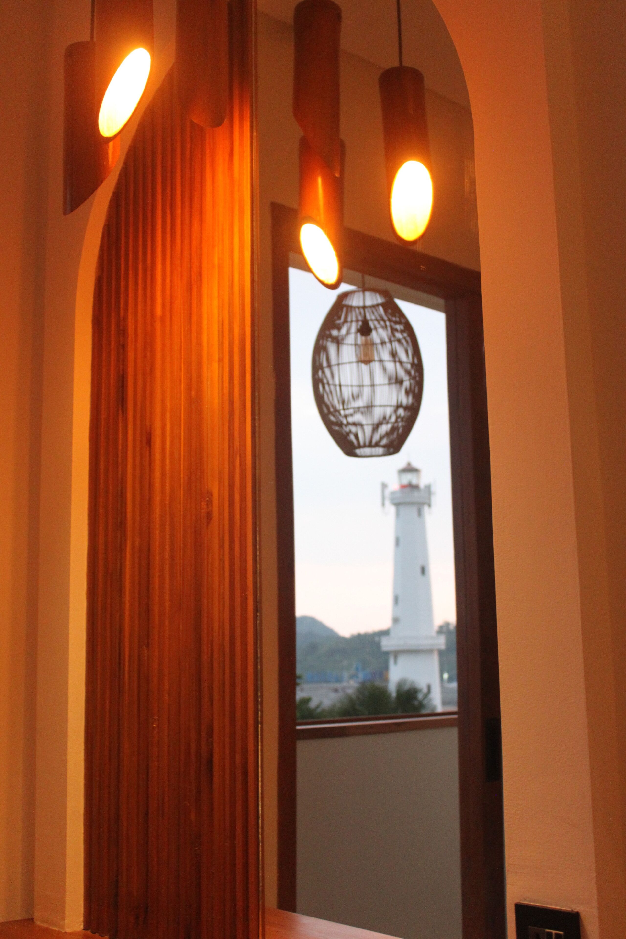 Une pièce avec un mur lambrissé en bois, une fenêtre donnant sur un phare et des lampes suspendues.