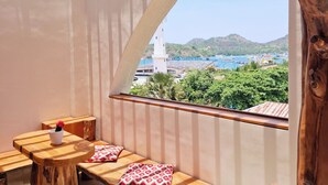 A wooden bench with cushions, a hanging light fixture, and a view of a coastal town. - OhJulia Hotel Komodo (Labuan Bajo)