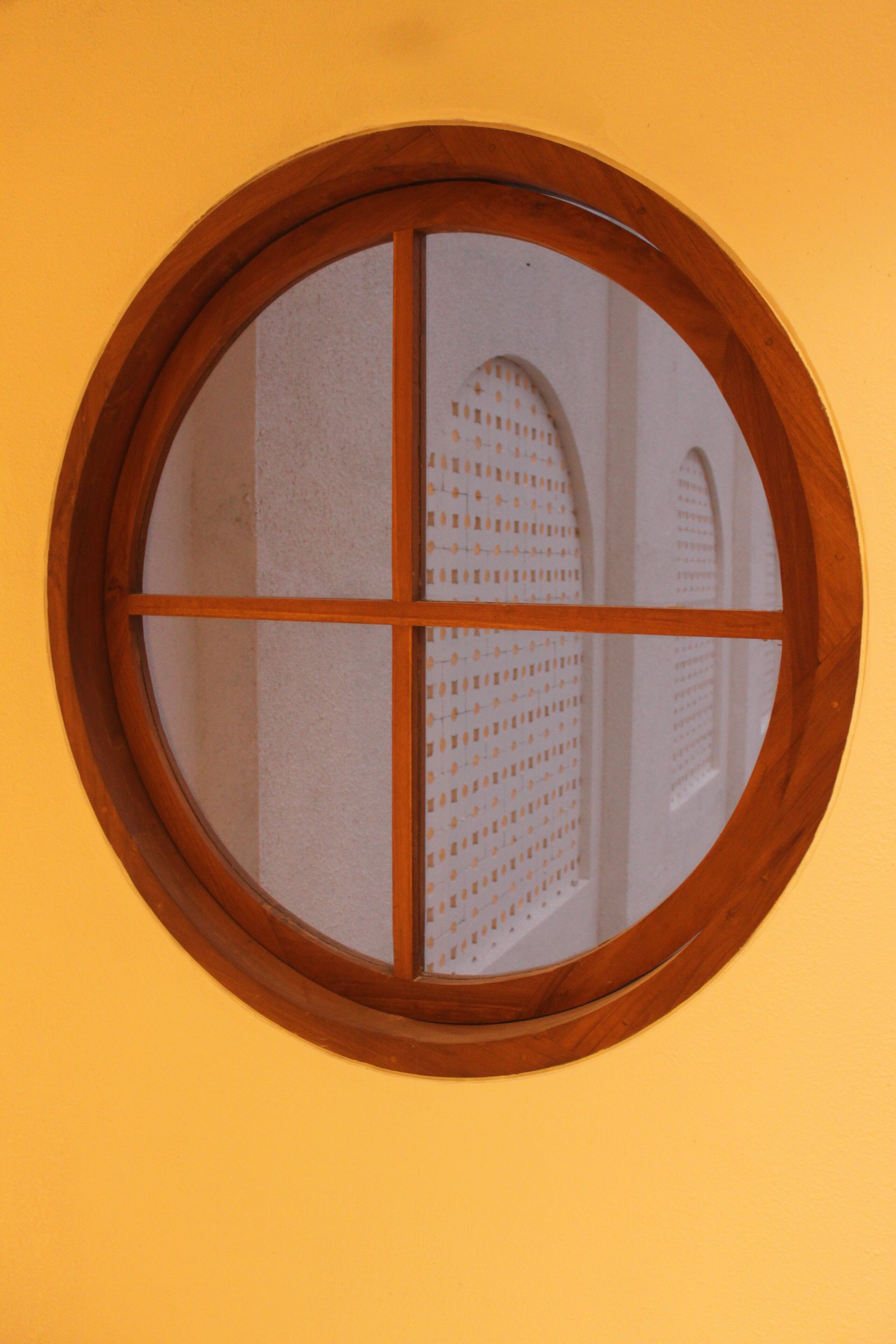 Una ventana redonda con marco de madera y un panel de vidrio esmerilado dividido en cuatro secciones.