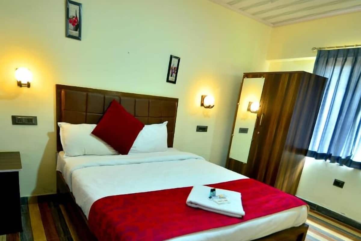 Una habitación de hotel con una cama, un plaid rojo y una mesita de noche.