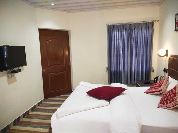 A hotel room with a bed, a television, a door, and a window with curtains. - Blossom Spring villa (Ooty)
