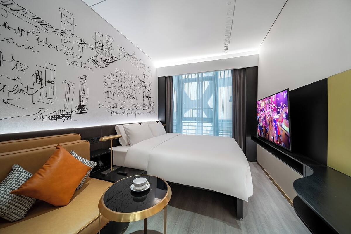 Ein modernes Hotelzimmer mit einem großen Bett, einem Fernseher, einer Couch und einer Wand mit architektonischen Skizzen.