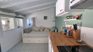 Ein gemütliches Schlafzimmer mit Bett, kleinem Nachttisch, Fenster mit Vorhang und einer Küchenzeile mit Ablage über der Arbeitsfläche.