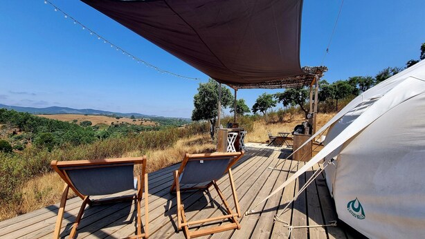 A wooden deck with two lounge chairs, a table, and a canopy providing shade. A tent is visible in the background. - Lotus Glamping Tent (São Luís)