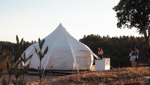 A white tent with a flat top and a small attached structure, set in a grassy area with trees in the background. - Lotus Glamping Tent (São Luís)