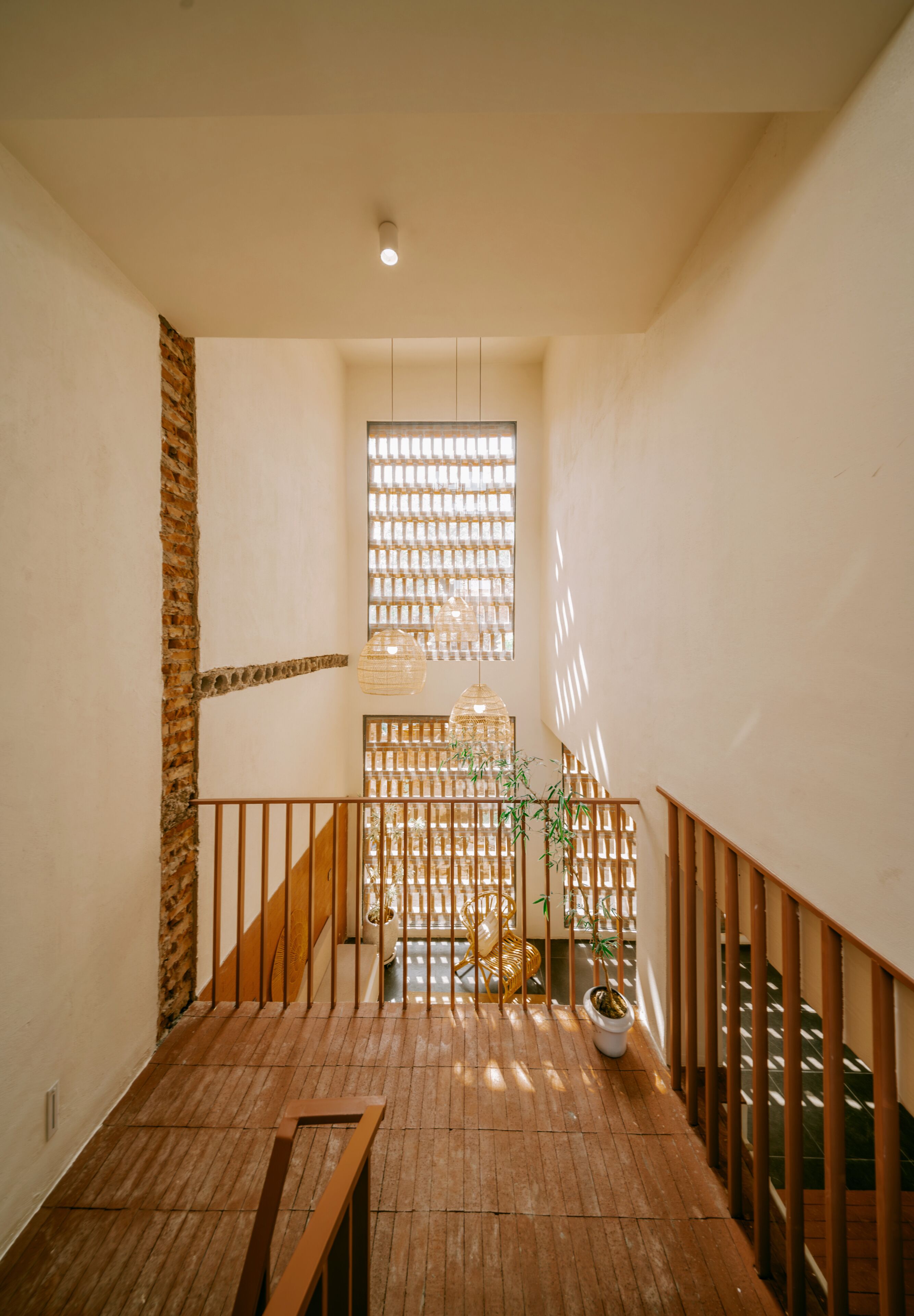 Un escalier en bois avec une rampe, un mur avec un motif en briques et une fenêtre avec des stores verticaux.