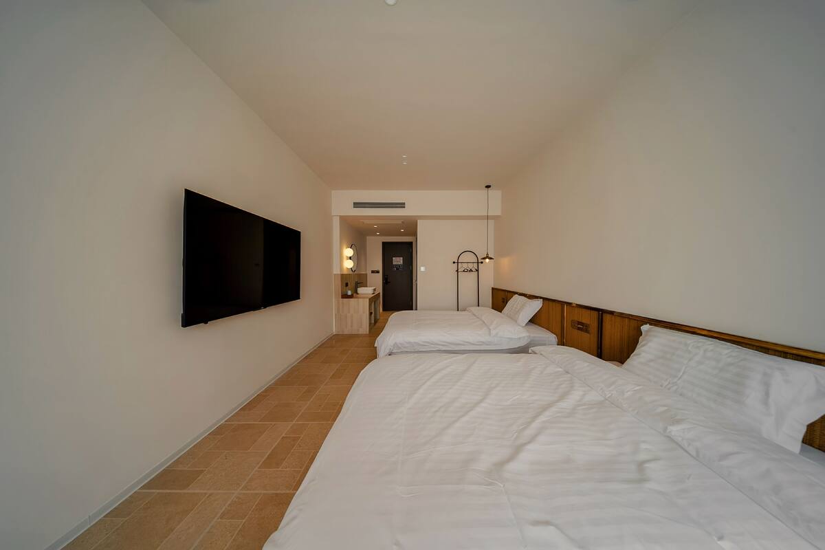 Quarto de hotel com uma cama grande, uma televisão de tela plana na parede e uma mesinha de cabeceira com luminária.