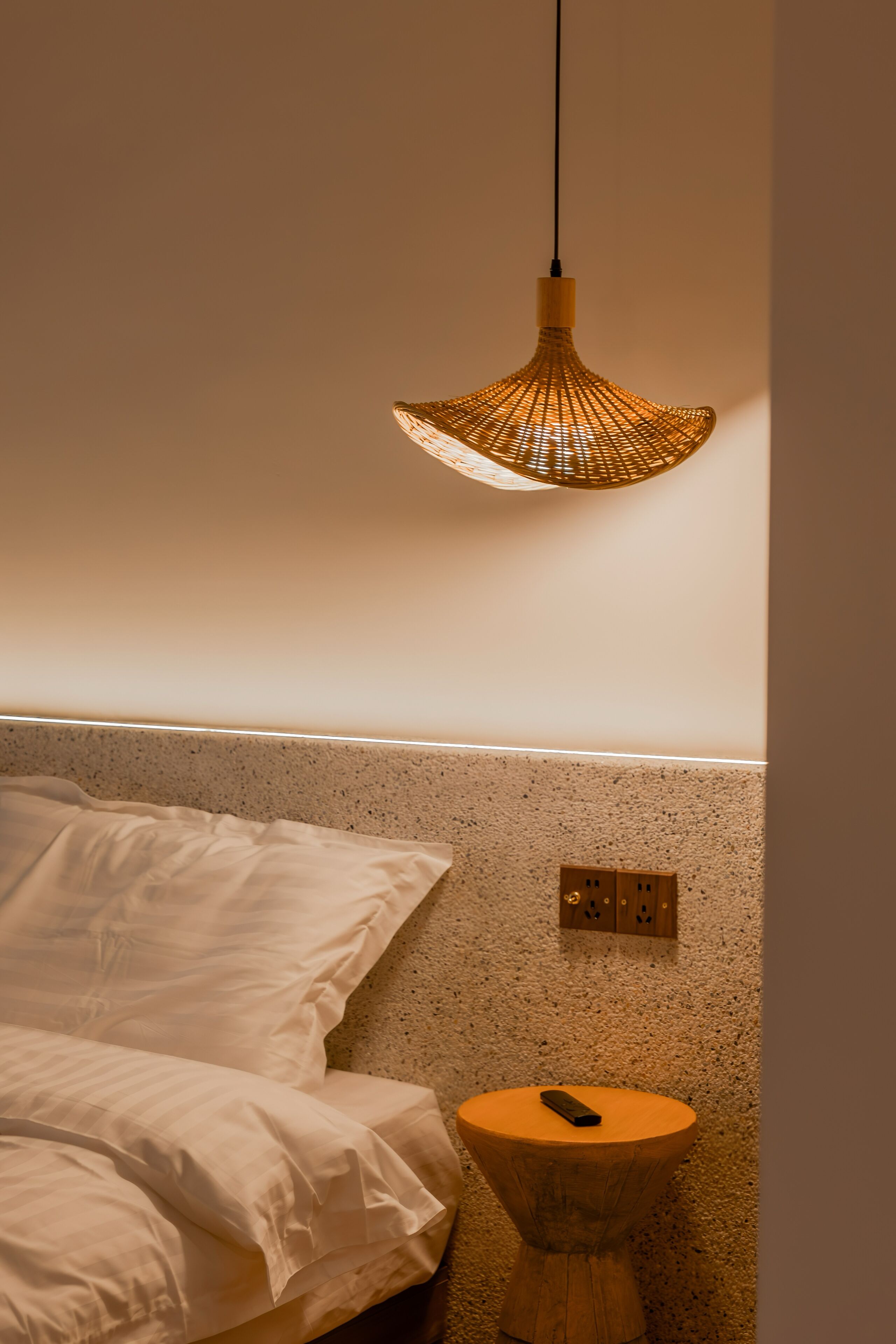 A bedroom with a bed, a bedside table, and a hanging light fixture.