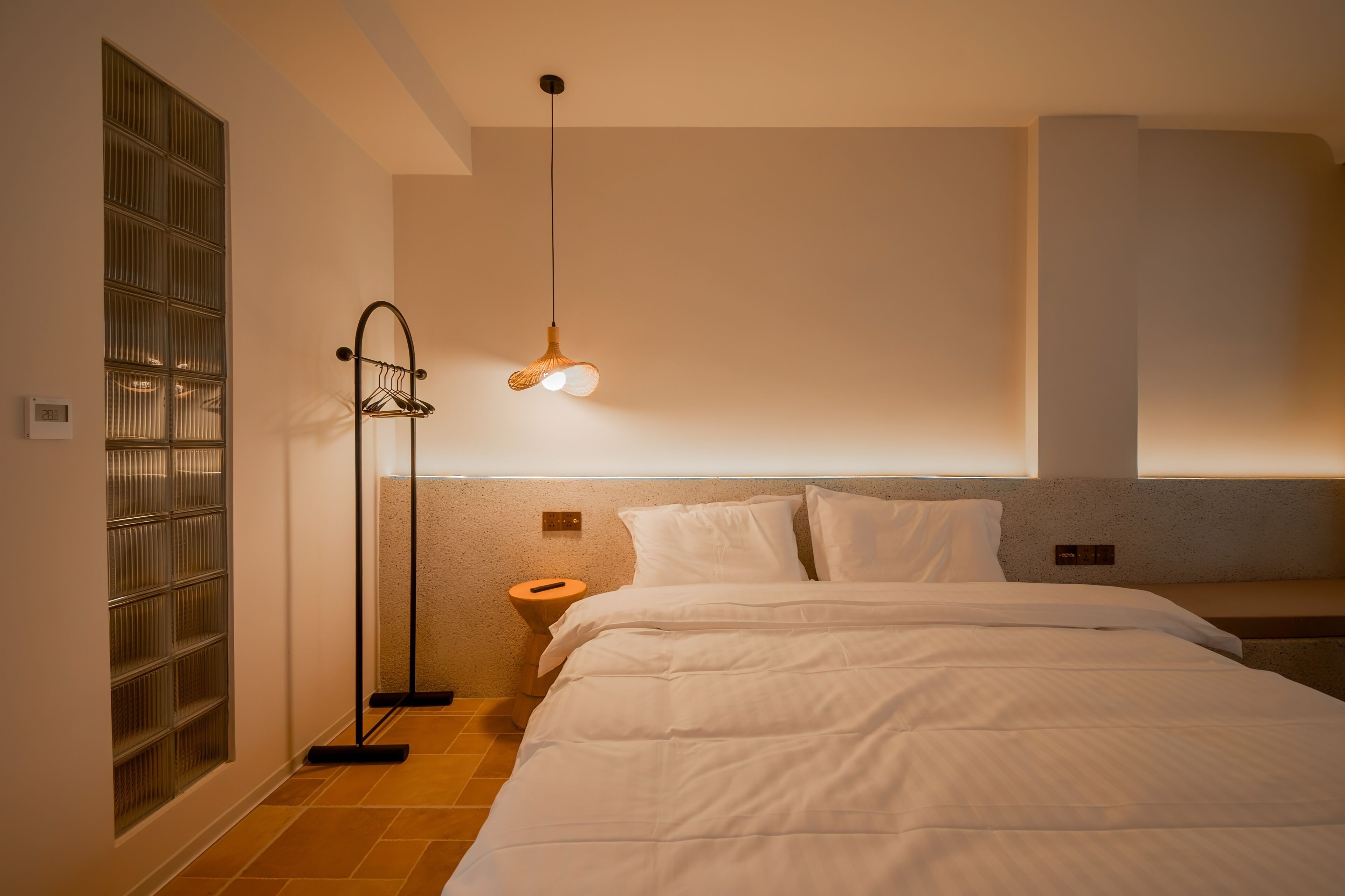 Une chambre d’hôtel comprenant un lit, une table de chevet, un luminaire suspendu et une étagère fixée au mur.