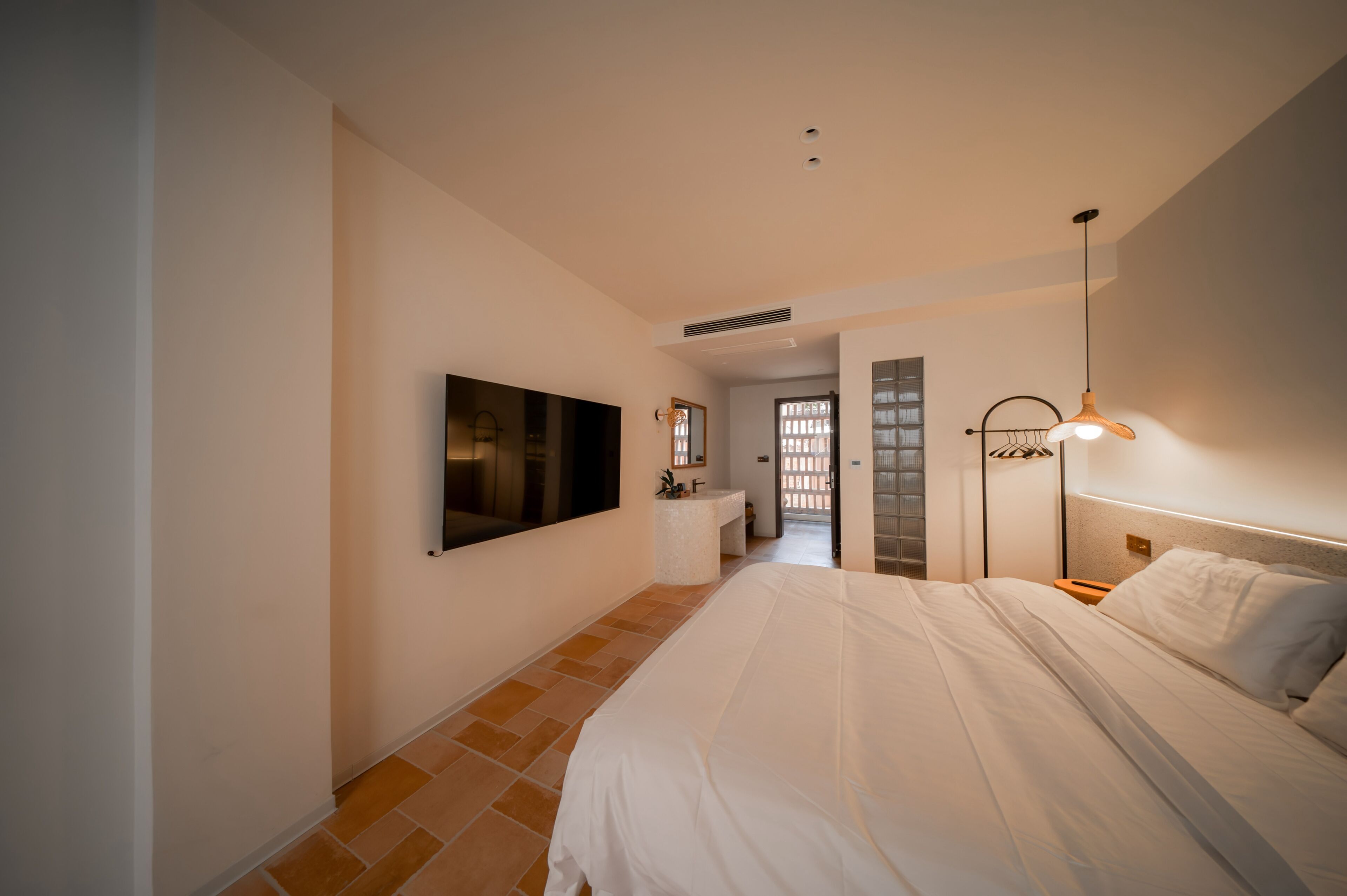 A bedroom with a bed, a TV mounted on the wall, a bedside table, and a lamp.