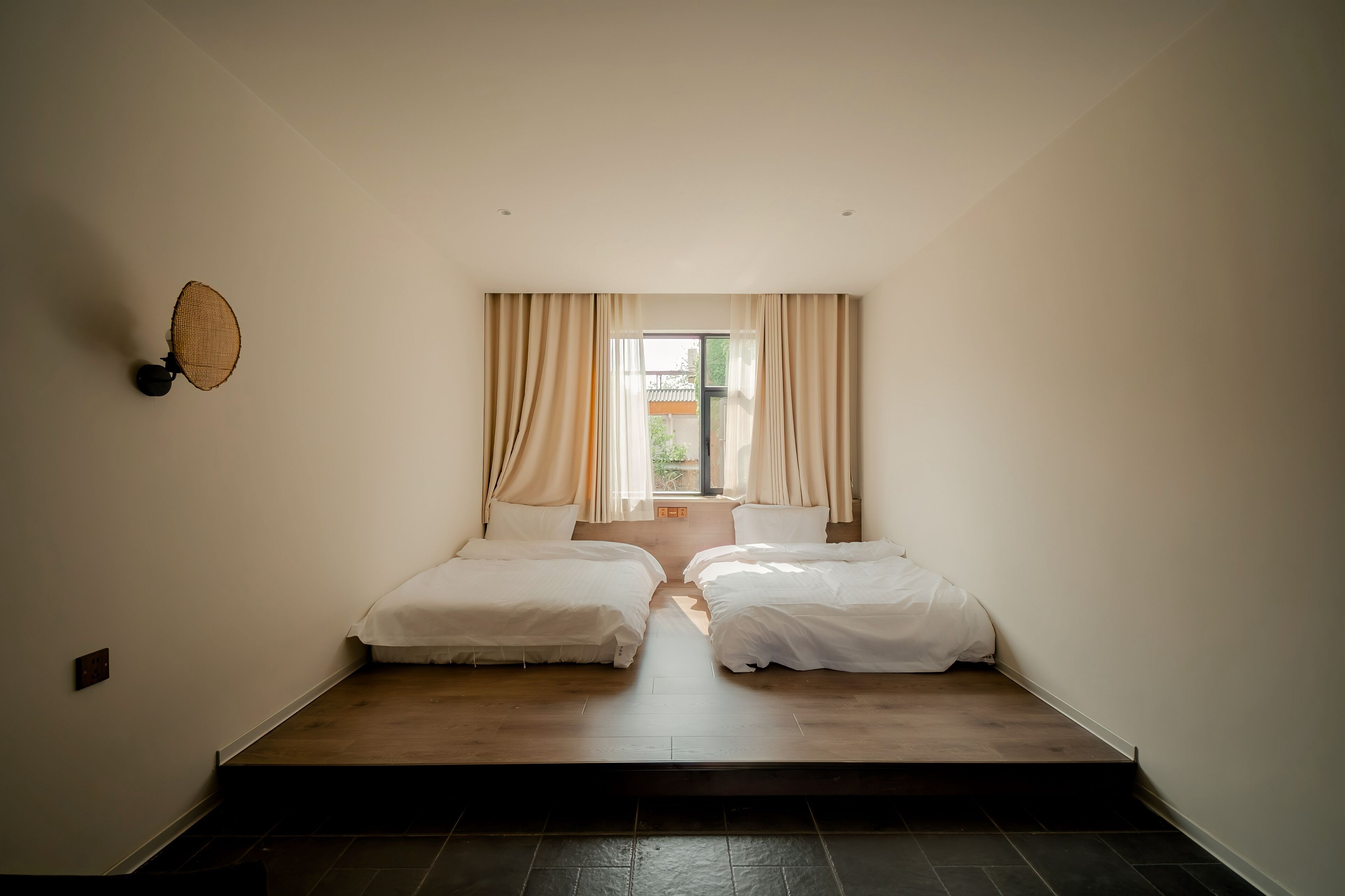 Una habitación con dos camas, una ventana con cortinas y una lámpara fijada a la pared.