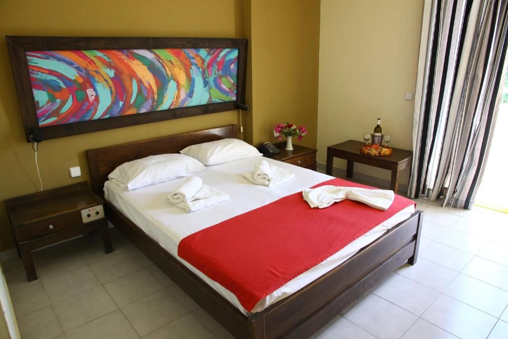 Habitación de hotel con cama, mesita de noche, cuadro y ventana con cortinas.
