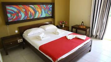 Habitación de hotel con cama, mesita de noche, cuadro y ventana con cortinas.