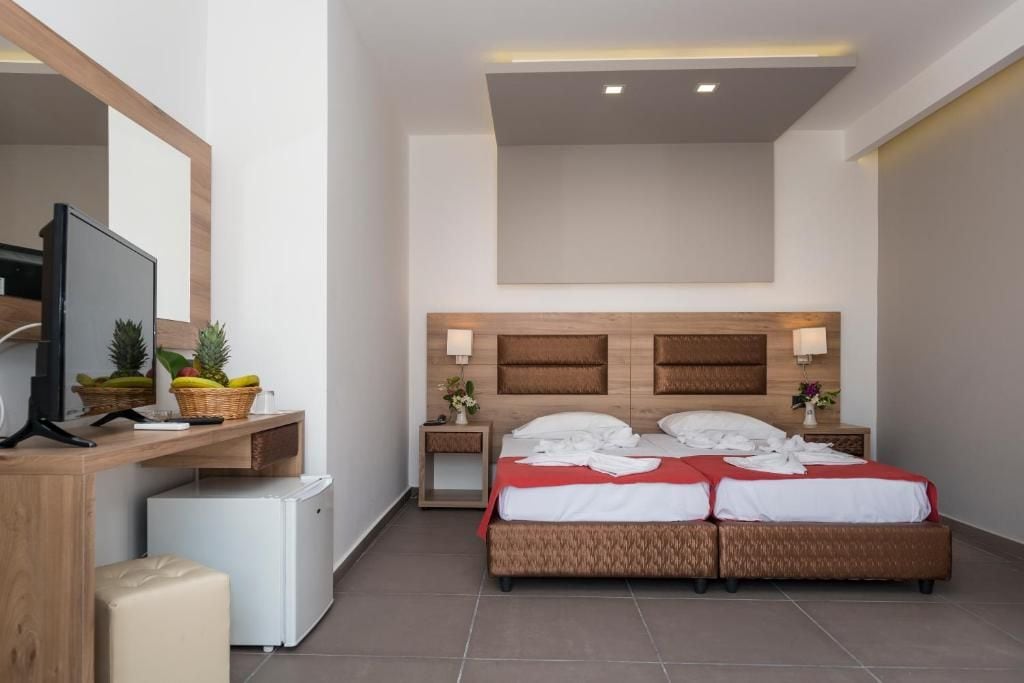A hotel room with a bed, a desk with a television, a small refrigerator, and a nightstand with a lamp.