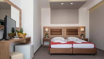 A hotel room with a bed, a desk with a television, a small refrigerator, and a nightstand with a lamp.