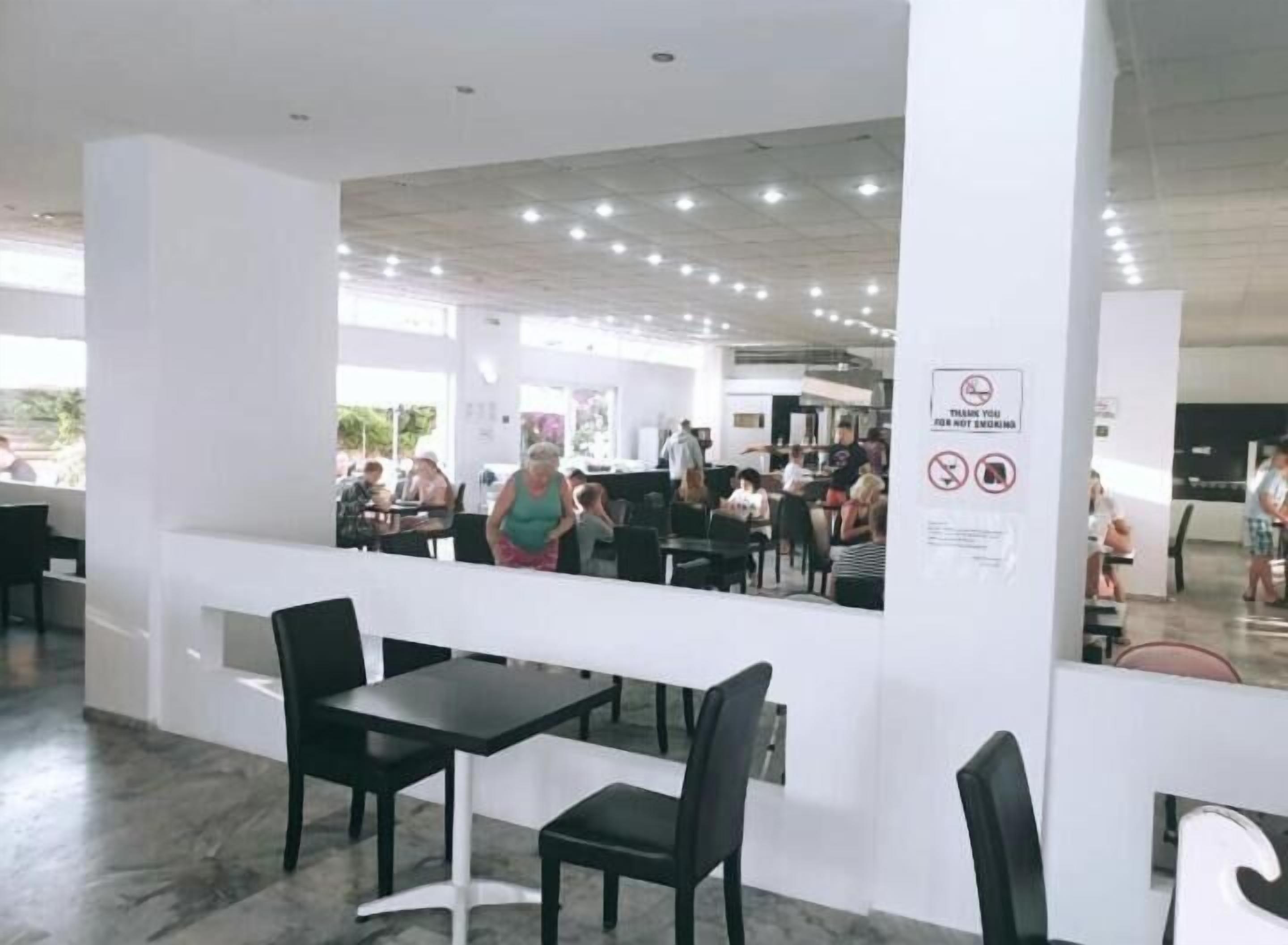 An indoor public space with tables and chairs, a white pillar with a sign, and a view of people in the background.